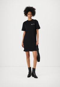 Svart bomulls t-shirtklänning med korta ärmar, rund halsringning och sidokilar. Bärs med svarta stövlar som går till anklarna och en crossbody-väska.