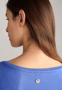 Blauwe katoenen T-shirt met een bootnek, voorzien van een klein merklabel op de achterkant. De stof lijkt zacht met een gladde textuur.