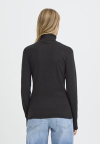 Pull noir à col roulé à manches longues, texture côtelée avec silhouette ajustée, porté avec un jean bleu. Vue de dos, design minimaliste, sans détails visibles.