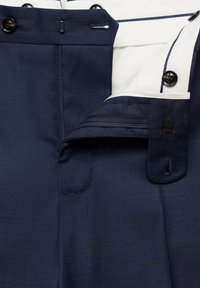 Pantalon bleu marine avec un tissu texturé, mettant en avant une fermeture éclair et un bouton, et une doublure intérieure blanche avec des accents contrastants.