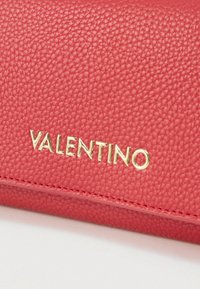Κόκκινο πορτοφόλι από δερματίνη με υφή, με ανάγλυφο χρυσαφί λογότυπο "Valentino" και λεπτομέρειες ραφής στις άκρες.