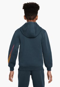 Felpa blu scuro con tasca a marsupio, polsini e orlo a costine. Presenta un motivo a righe colorate sulla manica sinistra e un cappuccio regolabile.