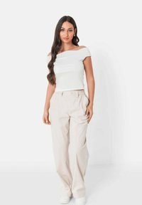 Witte off-the-shoulder top, beige losse broek, gladde stof, hoge taille met knoop, gecombineerd met witte sneakers.