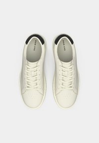 Paire de baskets basses blanches avec accents noirs au talon, bouts arrondis et lacets blancs, vues de dessus sur fond blanc.