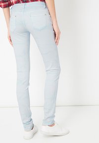 Jeans ajustados de color azul claro, hechos de denim, con una textura suave, bolsillos traseros con costuras decorativas y un ligero desvanecimiento.