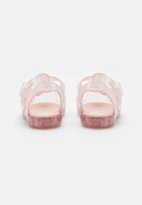Sandalias transparentes rosas con purpurina, parte trasera abierta y correas laterales para soporte. Textura lisa con una plantilla suave y suela plana.