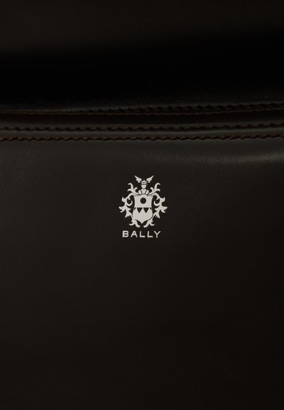 Rudas odos paviršius su iškilniu baltu "BALLY" logotipu ir herbo dizainu. Pabrėžtos smulkios siūlės prie kraštų, lygus paviršius.