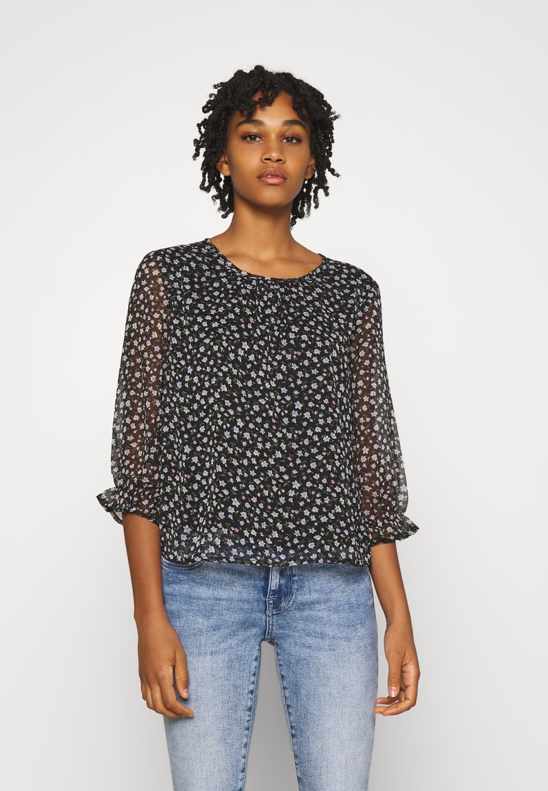 Blusa preta floral com tecido semi-transparente, mangas três quartos, punhos elásticos e um ajuste relaxado, apresentando pequenas flores multicoloridas.