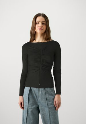 Zwarte langemouwen top met gerimpelde textuur aan de voorkant, ronde hals en ritssluiting op de rug, gecombineerd met lichtblauwe geplisseerde broek.