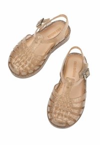Sandali in gel glitter oro con design a strappo, punte scoperte, cinturino posteriore e dettagli con fibbia; materiale liscio e suole testurizzate.