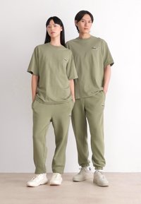 Olijfgroene bijpassende t-shirts en sweatpants van een katoenmix, met een logoaccent op de linkerkant van de borst en heup. Textiel: zacht, soepel.