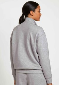 Grijze sweatshirt met een hoge kraag, zachte textuur en ribbelmanchetten. Kenmerkt zich door een ontspannen pasvorm, achternaaddetail en bijpassende broek zichtbaar.