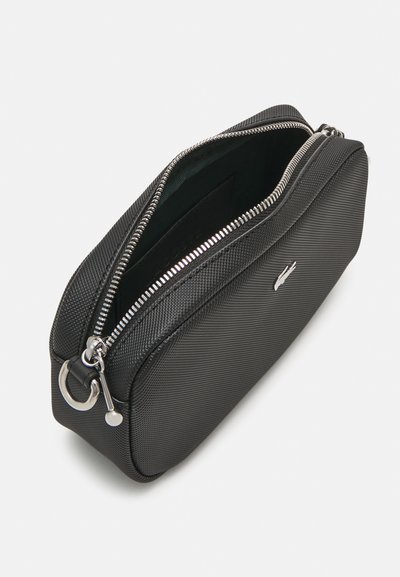 Pochette noire zippée avec un extérieur texturé, dotée d'une fermeture éclair et d'accents argentés. Doublure intérieure verte. Forme compacte et rectangulaire.