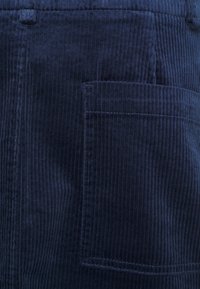 Tissu en velours côtelé marine présentant des côtes verticales, une surface texturée et une poche à rabat sur le côté droit.