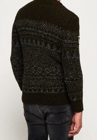 Tumma vihreä neulottu villapaita, jossa on teksturoituja kuvioita ja resorikaulus. Harmaat yksityiskohdat koristavat olkapäitä ja hihoja.