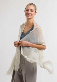 Lightweight, sheer scarf in cream color, featuring frayed edges, draping elegantly over a blue top. Soft texture, flowing design.