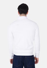 Maglione bianco a maglia con maniche lunghe, polsini e orlo a coste, indossato sopra una camicia con colletto. La parte posteriore è semplice, senza motivi o dettagli visibili.