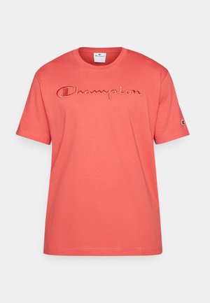 Camiseta de algodón color coral con mangas cortas, con el logo bordado de "Champion" en el pecho y un pequeño logo en la manga.