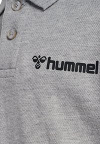 Szara koszulka polo z teksturowaną tkaniną, listwą na guziki oraz czarnym logo "hummel" z motywem pszczoły po lewej stronie.