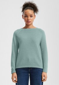 Pull en maille côtelée bleu clair avec un col rond et des manches longues. Le tissu texturé présente des rayures horizontales et des poignets ajustés.