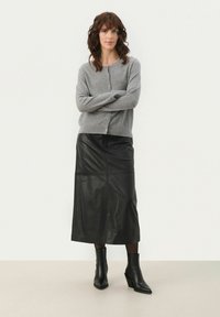 Gray cardigan with buttons, paired with a black leather midi skirt. Model wears black ankle boots with a pointed toe. Smooth textures throughout.