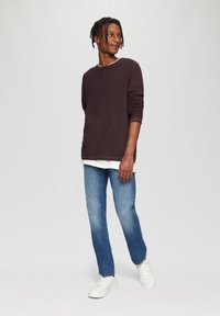 Pull long-sleeve bordeaux foncé sur une chemise blanche, associé à un jean bleu clair et des baskets blanches. Texture lisse et coupe décontractée.