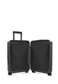 Valise noire zippée avec une coque rigide, dotée d'une poignée extensible, de quatre roues et de compartiments intérieurs en maille. Texture lisse.