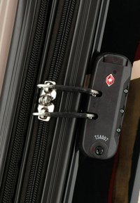 Valigia nera rigida con zip, dotata di un lucchetto a combinazione con TSA, chiusura in metallo argentato e superficie liscia e lucida.