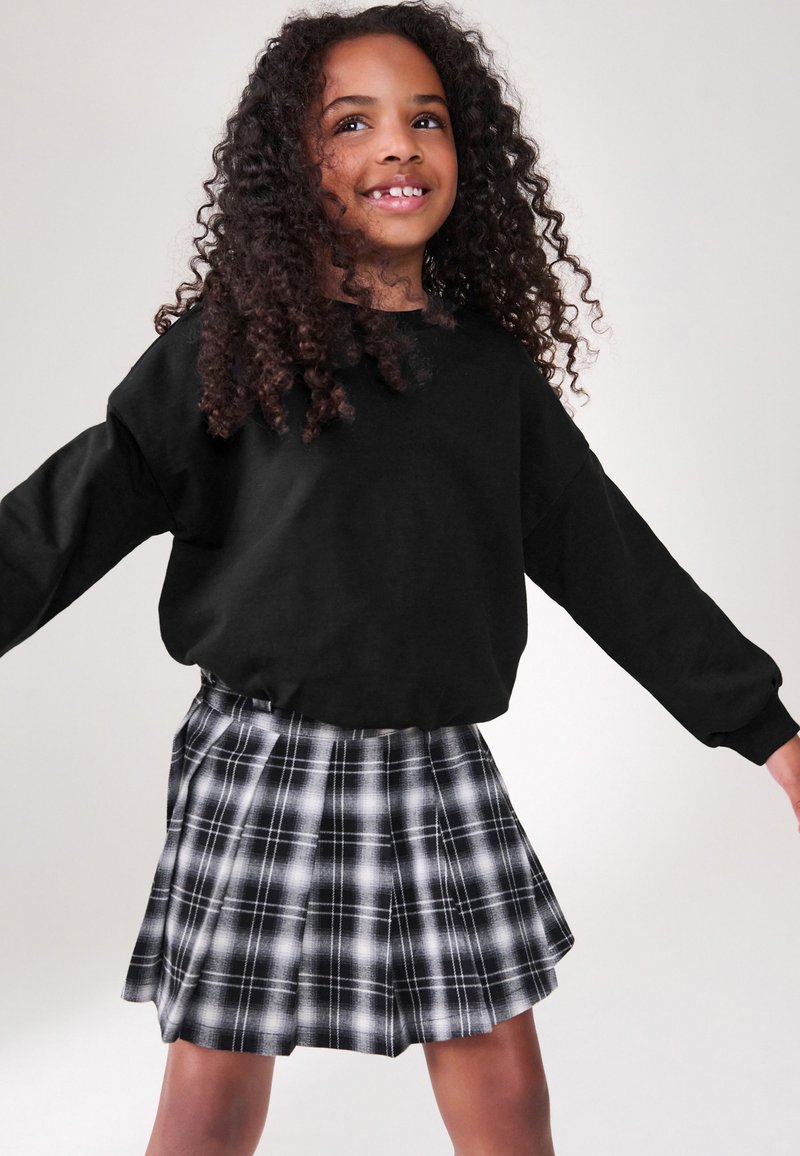 Juodas trumpintas džemperis derinamas su juodos ir baltos spalvos languota klostuota suknele. Audinys minkštas, su lygiu paviršiumi ir ilgomis rankovėmis.