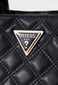 Borsa a tracolla nera in pelle trapuntata con logo triangolare bordato in oro e dettagli neri, che mette in evidenza una superficie testurizzata e un motivo cucito.