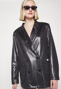 Kaksikaupaheline särk, läikivas mustas materjalis, millel on suured nööbid, soonikkraagud ja väike valge logo vasakul taskul.