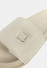 Sandal in bianco con un upper imbottito caratterizzato da un logo metallico quadrato, texture liscia e un plantare sagomato.