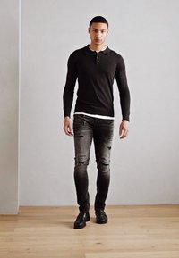Sort langærmet polo-shirt med tre-knaps knaplukning, parret med slidte mørkegrå slim-fit jeans og sorte klassiske sko.