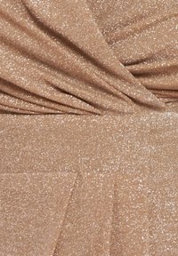 Glittrande beige tyg med fin glittrig textur som samlas i mjuka veck och plisseringar, vilket skapar en draperad effekt.