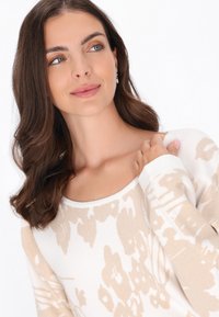 Sweter robiony na drutach w kolorze kremowym z beżowym kwiatowym wzorem, z okrągłym dekoltem, długimi rękawami i miękką teksturą. Prosty design z minimalnymi detalami.