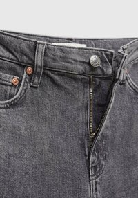 Jean en denim gris foncé dézippé avec bouton en métal et rivets en cuivre, mettant l'accent sur la taille et la zone de la fermeture éclair.