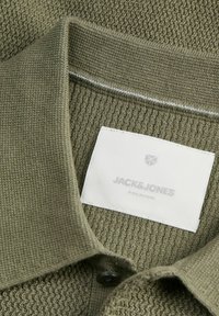 Col polo en tricot texturé vert avec une étiquette blanche cousue comprenant un logo discret et le nom de la marque.