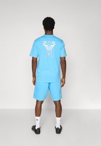Light blue short-sleeve t-shirt with a white and pink graphic on the back, paired with matching shorts. Worn with white socks and black shoes.