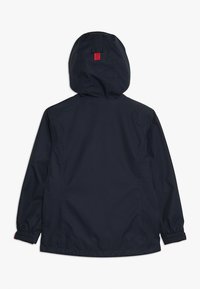 Giacca impermeabile blu navy con cappuccio, polsini elasticizzati e una etichetta rossa sul retro, con texture liscia e design semplice.