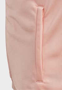 Vaaleanpunaiset urheilushortsit, joilla on sileä pinta, sivutasku ja ommellut korostukset kestävyuden vuoksi.