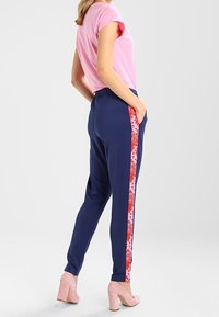 Marina joggers med en rosa blommig sidremsa, elastisk midjeband och två sidofickor, kombinerat med en kortärmad rosa t-shirt.