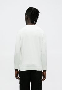 Valge pika varrukaga kampsun ümmarguse kaelusega, soonikkoes varrukaotste ja alumise äärega, pehme kangaga ning lõdva istuvusega. Näidatud tagantvaade.