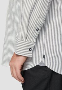 Chemise rayée avec des rayures verticales bleu et blanc, poignets boutonnés, tissu texturé, ourlet incurvé et une petite étiquette logo près de l'ourlet.