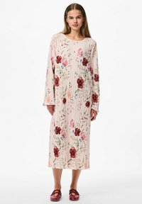 Haljina dugih rukava s cvjetnim uzorkom u svijetlo ružičastoj boji s plisiranjem; sadrži crvene i ružičaste cvjetove s zelenim naglascima. Nosena s bordo cipelama.