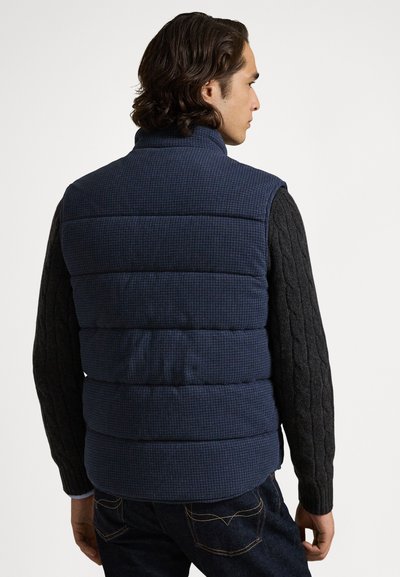 Σκούρο μπλε γιλέκο με καρό σχέδιο, ψηλό γιακά και μαύρα πλεκτά μανίκια με σχέδιο καλωδίου. Πυκνή, καπιτονέ υφή. Casual εφαρμογή.