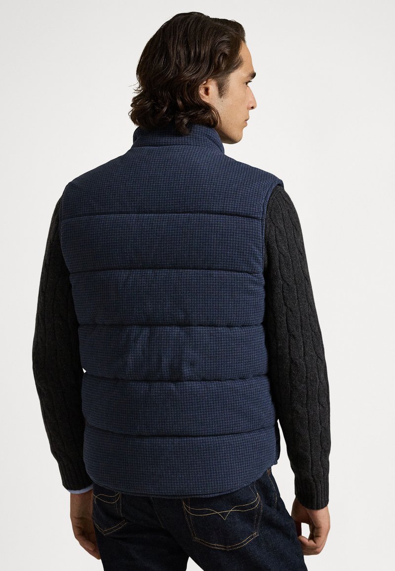 Marineblaue Steppweste mit Karomuster, hohem Kragen und schwarzen Strickärmeln mit Zopfmuster. Dicke, gesteppte Textur. Legere Passform.