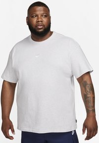 Grijze korte mouwen t-shirt van katoen. Heeft een klein wit Nike-logo op de borst en een losse pasvorm. De textuur lijkt zacht en casual.