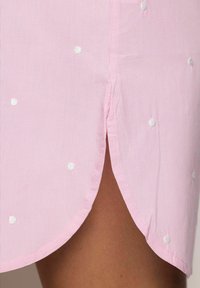 Camicia a righe rosa chiaro con pois bianchi, con orlo arrotondato e spacchi laterali. Tessuto in cotone morbido con una finitura netta.