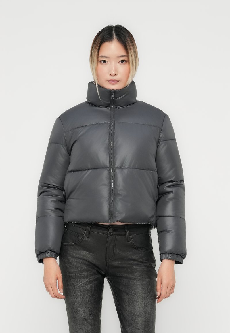 Cropped grey puffer jacket with high collar, full zipper, and quilted texture. Model wears it with black jeans against a plain background.