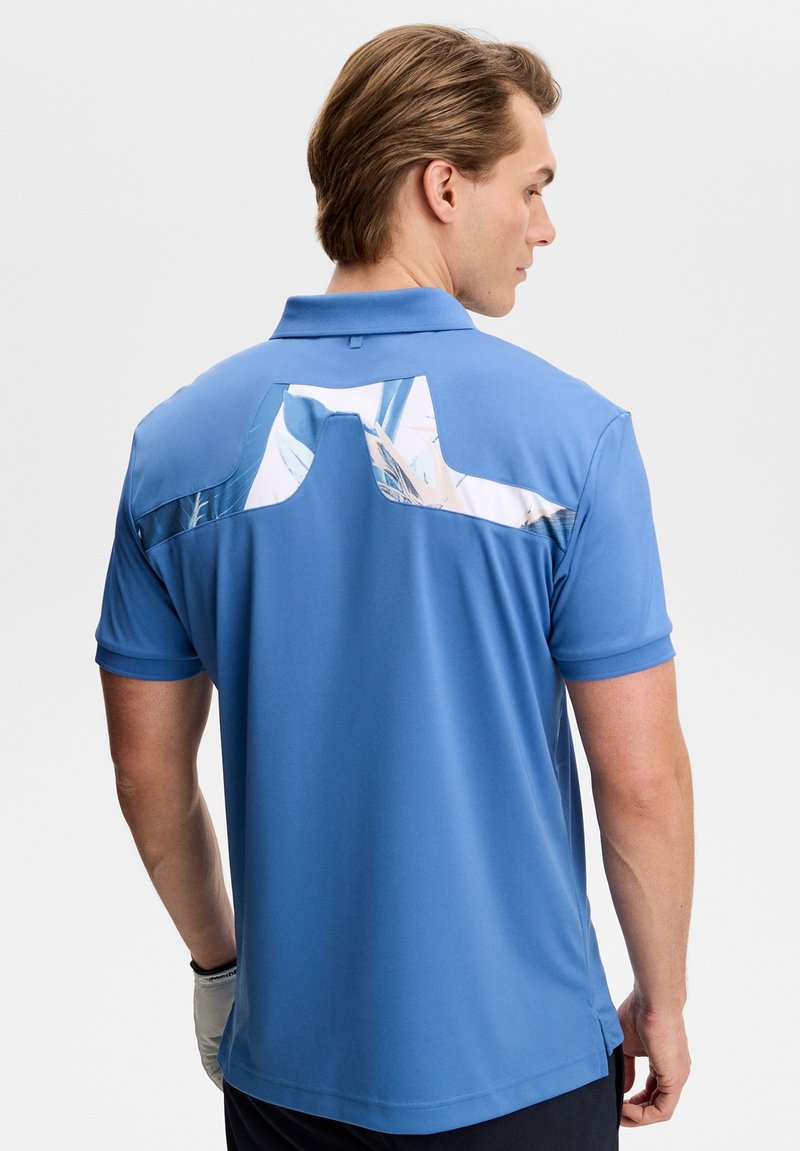 Polo bleu pour homme à manches courtes, avec un panneau arrière unique à motifs blancs et bleus, fabriqué en tissu léger.
